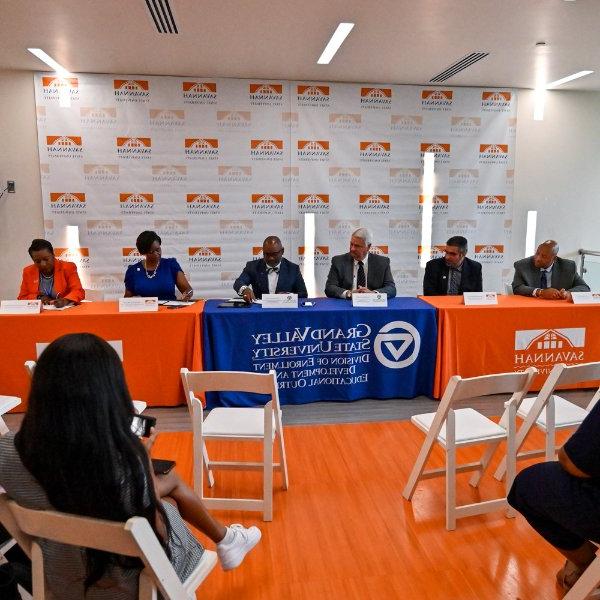 six people seated at table signing papers, with table drapes of savannah state university and GVSU