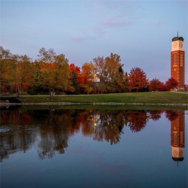 Trees with fall color are also reflected in a pond. The carillon is in the background.